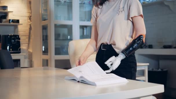 Una ragazza sta scorrendo pagine di libri con un braccio protesico. Braccio robotico simile a quello umano . — Video Stock
