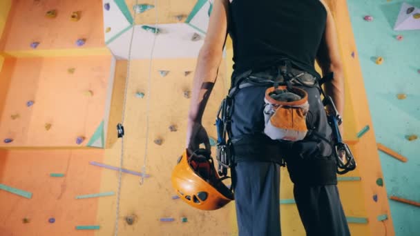 Backside view of an equipped mans lower body standing in front of a climbing wall — Stock Video