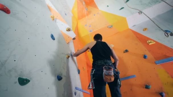 Corner of a bouldering wall starts getting climbed by an equipped man — Stock Video