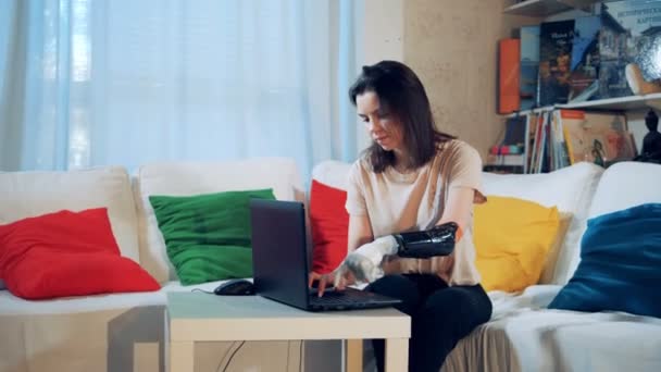 Chica discapacitada trabaja con un ordenador portátil, usando prótesis de mano, de cerca . — Vídeos de Stock