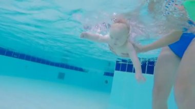 Şirin bebek yüzme havuzunda su altında yüzüyor.