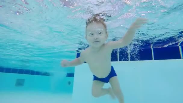 Un bebé flotando bajo el agua en una piscina, de cerca . — Vídeo de stock