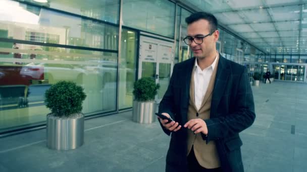 Empresário masculino gerente caminha e tipos em um telefone, sorrindo, close-up . — Vídeo de Stock