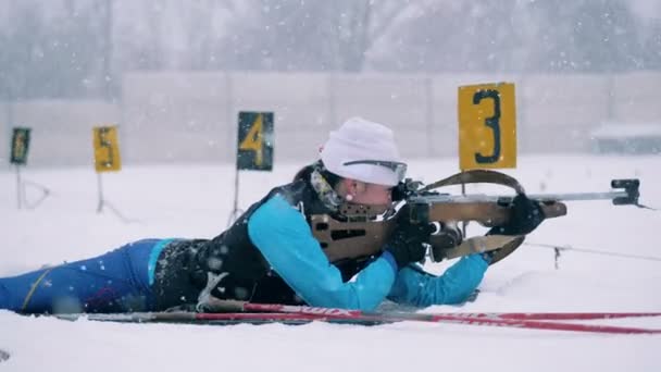Female biathlete is lying in the shooting zone with a rifle — Stock Video