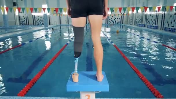 Piscine et un homme avec une jambe prothétique debout sur un bloc de départ — Video