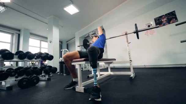 Salle de gym et un homme avec une jambe robotisée soulevant un bar — Video