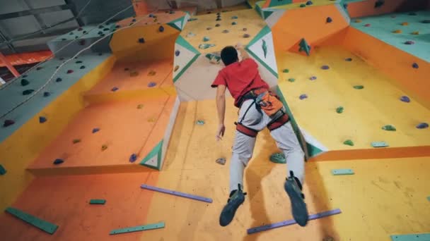Un escalador cuelga en una pared de entrenamiento, vista inferior . — Vídeo de stock