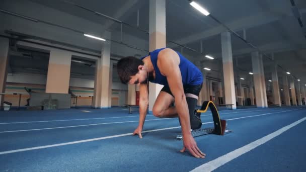 El hombre comienza a correr en una pista, con la pierna artificial, vista lateral . — Vídeos de Stock