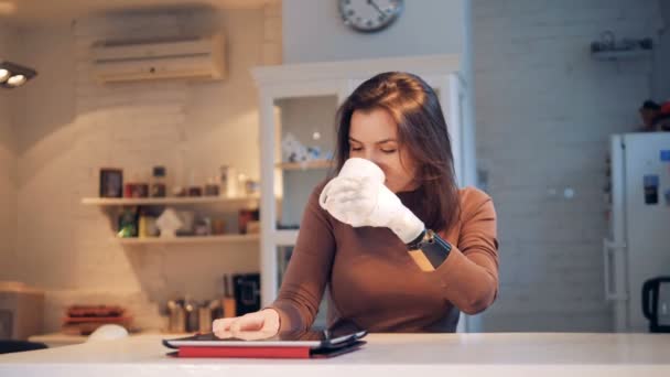 一位拿着仿生手的女士从杯子里喝水, 操作着一台平板电脑 — 图库视频影像