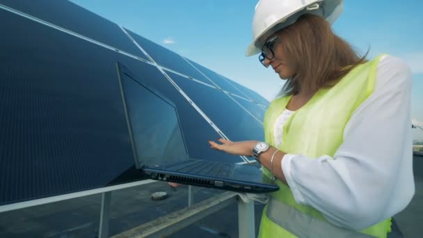 Una mujer sonríe ante la cámara mientras está de pie cerca de los paneles solares, de cerca . — Vídeo de stock