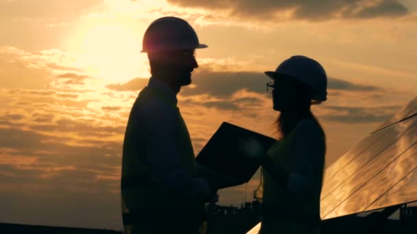 Muž a žena stavební dělníci mluvit o západu slunce pozadí, boční pohled.