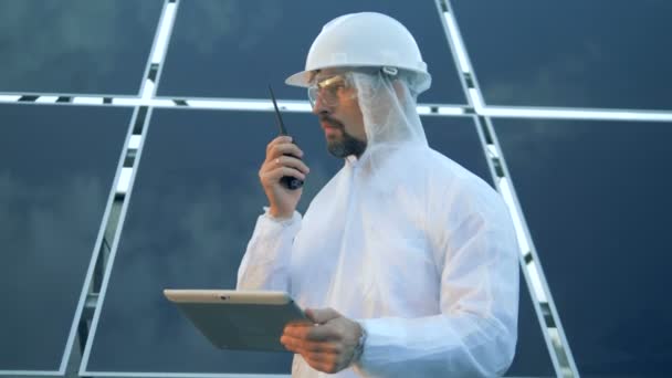 Trabalhador masculino usa um walkie-talkie, de pé perto de baterias solares, close-up . — Vídeo de Stock