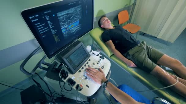 Egy orvos ellenőrzi mans térd, használ egy ultrahang gép, felülnézet. — Stock videók