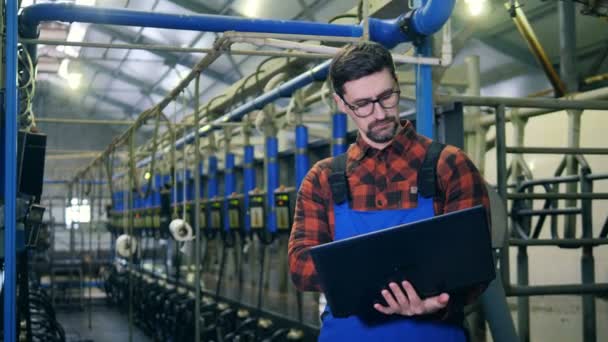 Um homem digita em um laptop, de pé perto do equipamento do galpão, de perto . — Vídeo de Stock