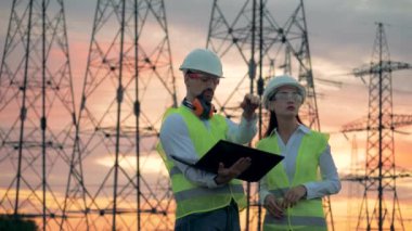 Bir erkek ve bir kadın ile bir laptop güç hattı direkleri çalışıyor. Mühendis yenilenebilir enerji geliştirme üzerinde çalışıyor.