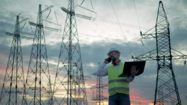 Erkek mühendis güç hatları yakınındaki bir telefonda konuşuyor