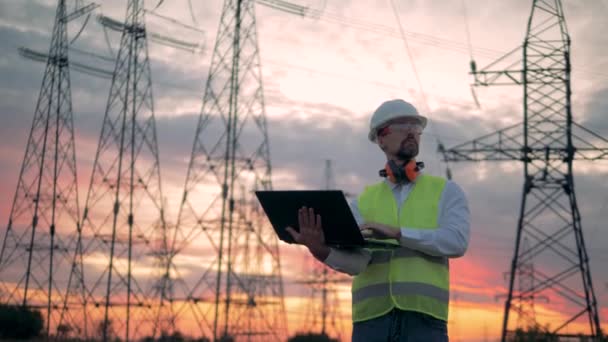 Tours de lignes électriques et un ingénieur masculin au coucher du soleil — Video