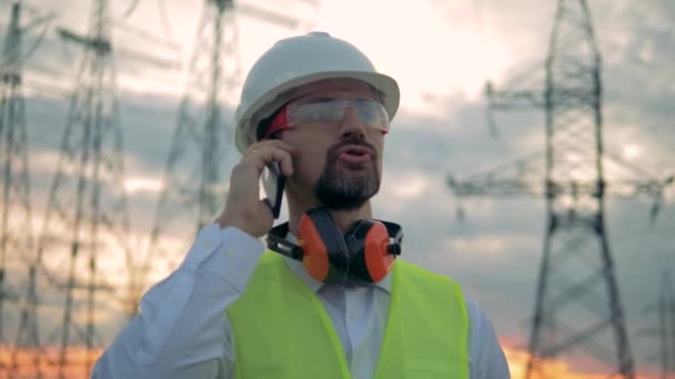 Close up de um cara engenheiros do sexo masculino enquanto fala em um telefone perto de linhas de energia — Vídeo de Stock
