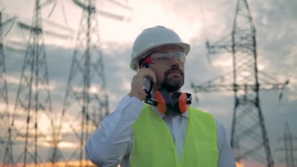 Técnico masculino está terminando uma fonecall e sorrindo ao estar perto de linhas de energia — Vídeo de Stock