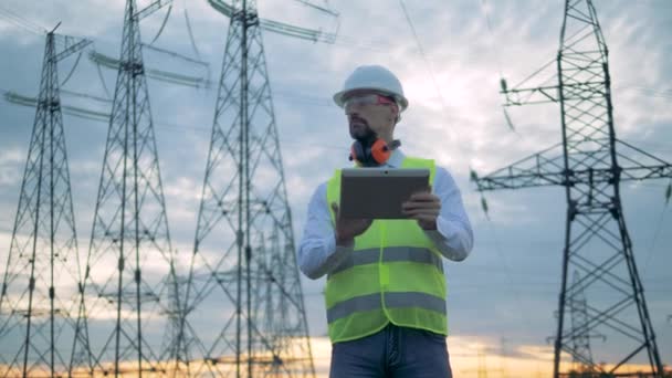 Torres de linhas elétricas e um técnico do sexo masculino operando um tablet — Vídeo de Stock