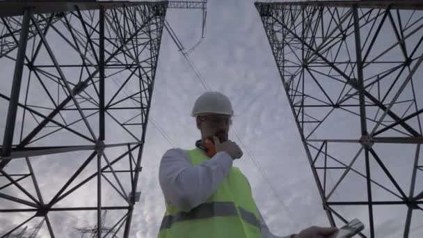 Bulutlu gökyüzü ve uzun boylu Etl kule arasında çalışan bir erkek teknisyen — Stok video