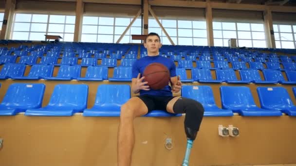 Koszykarz z proteza nogi siedzi na ławce, z bliska. — Wideo stockowe