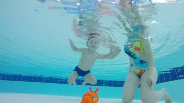 Bebé está tomando un juguete de debajo del agua de una piscina bajo el control de las mamás — Vídeos de Stock