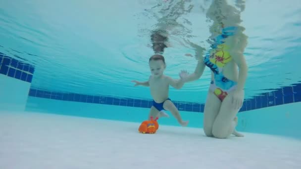 Mujer ayuda a un niño a levantar un juguete desde el fondo de la piscina — Vídeos de Stock