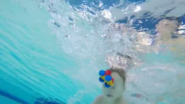Мальчик плавает под водой со своими игрушками в бассейне — стоковое видео