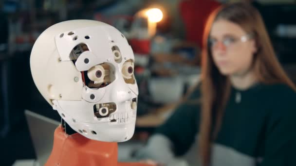 Primer plano de los gestos faciales de un cyborg con una señora trabajando en el fondo — Vídeos de Stock