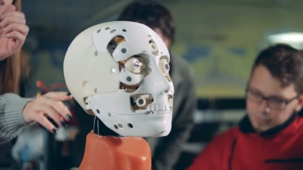 Детальный обзор лица робота со специалистами, говорящими на заднем плане — стоковое видео