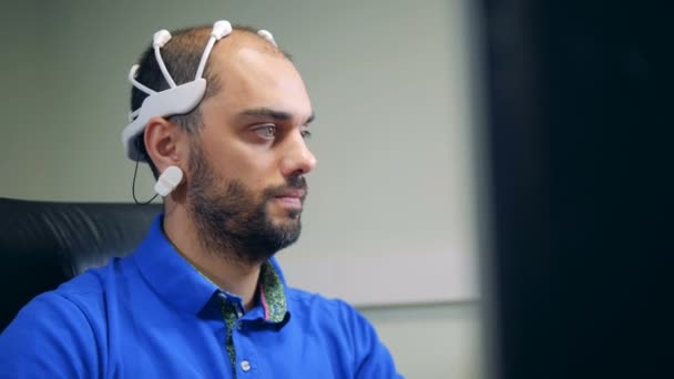 Un hombre en un auricular de escaneo de ondas cerebrales está operando una computadora — Vídeo de stock