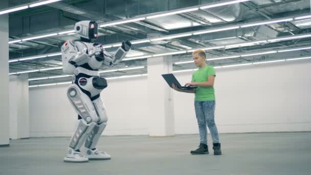 Tonårspojke manipulerar en robot med sin laptop — Stockvideo