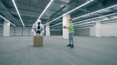 Genç çocuk bir karton kutu kaldırmak için bir robot rehberlik