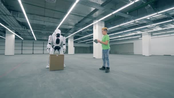Ragazzo adolescente sta guidando un robot per sollevare una scatola di cartone — Video Stock