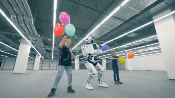 Människolik robot dansar med två barn hålla ballonger — Stockvideo