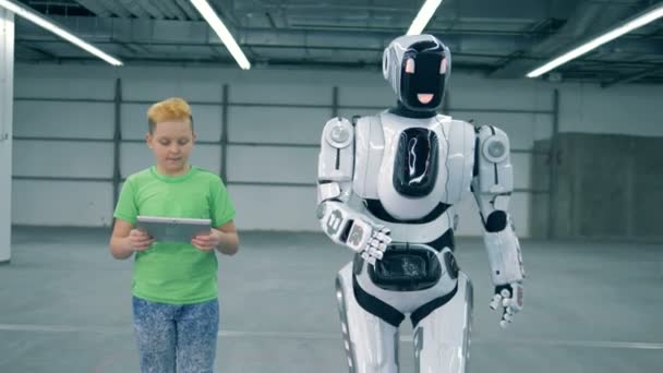 Boy with a tablet is manipulating a robot into walking — Stock Video