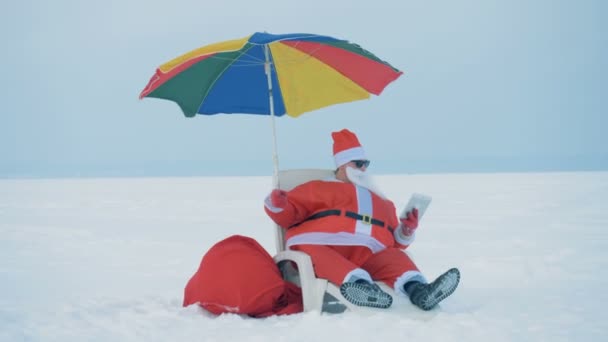 Claus sitter på en solstol och arbetar med en surfplatta, närbild. — Stockvideo