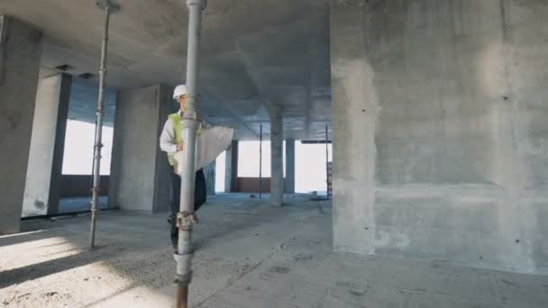 Ένας άνδρας που κρατά blueprint ενώ το περπάτημα σε ένα κτίριο, εσωτερικη. — Αρχείο Βίντεο