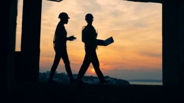 İki işçi bir projeyi tartışmak, gün batımı bir arka plan üzerinde duran, arkadan görünüm. 