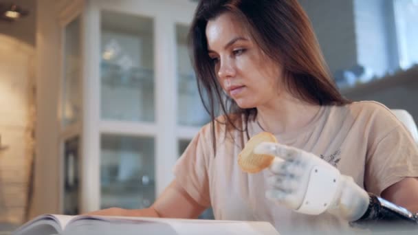 Mulher bonita com uma mão biônica está lendo e comendo um biscoito — Vídeo de Stock