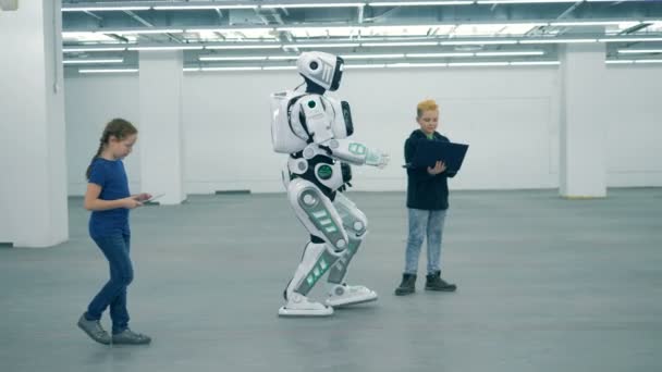 Концепция будущего. Дети смотрят, как дроид ходит во время работы с компьютерами. Современный киборг с детьми — стоковое видео