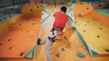 Bir adam donanımları, alt görünümü güvenliğini sağlama ile bir duvara tırmanıyor.