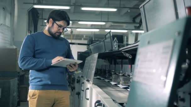 Una persona digita su un tablet durante il controllo delle attrezzature di stampa, da vicino . — Video Stock