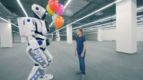 Robô dá balões e sua mão para uma menina em uma unidade de armazenamento — Vídeo de Stock