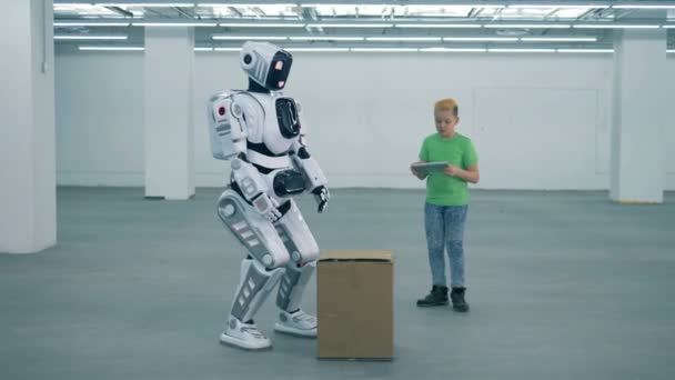 Tonårspojke kommandon en robot att lyfta en låda — Stockvideo