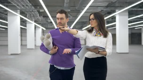 Salón vacío con una mujer y un hombre arquitectos caminando por él — Vídeos de Stock