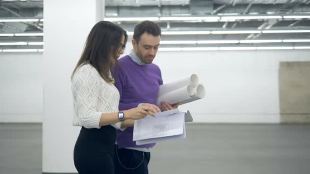 Una mujer y un hombre caminan por el pasillo con dibujos arquitectónicos — Vídeos de Stock