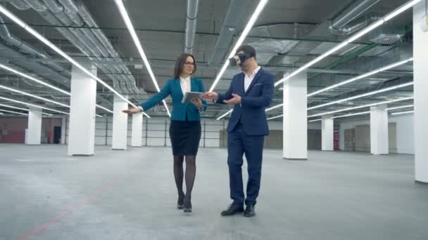 Женщина-агент показывает пустое офисное помещение мужчине в VR-очках — стоковое видео
