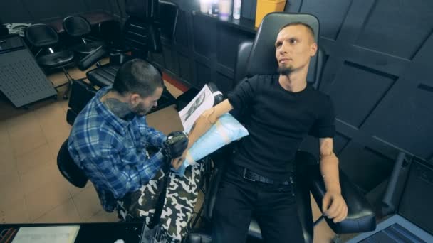 Un studio avec un artiste masculin faisant un tatouage sur mans main prothétique — Video